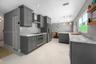 Kitchen featuring dark grey shaker-style cabinetry, stone-finish countertops with matching backsplash, stainless steel appliances including a chimney-