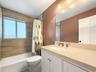 Bathroom featuring a stone-finish countertop with an integrated basin, white shaker-style vanity cabinetry, wood-finish wall tile surrounding the bath