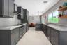 Kitchen featuring charcoal-toned cabinetry, light-toned stone-finish countertops, full-height stone-finish backsplash, stainless steel appliances, and