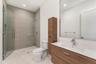 Bathroom featuring a floating wood-finish vanity with an integrated sink, a frameless glass walk-in shower with textured tile surround, a vertical woo