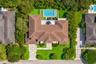 Aerial perspective of a property featuring a tiled roof, rectangular swimming pool, stone paver driveway, manicured lawn, and mature perimeter landsca