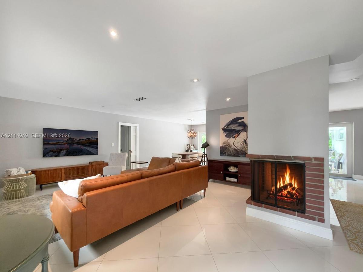 Open-concept living space featuring large-format tile flooring, recessed lighting, and a dual-sided brick fireplace with a glass enclosure