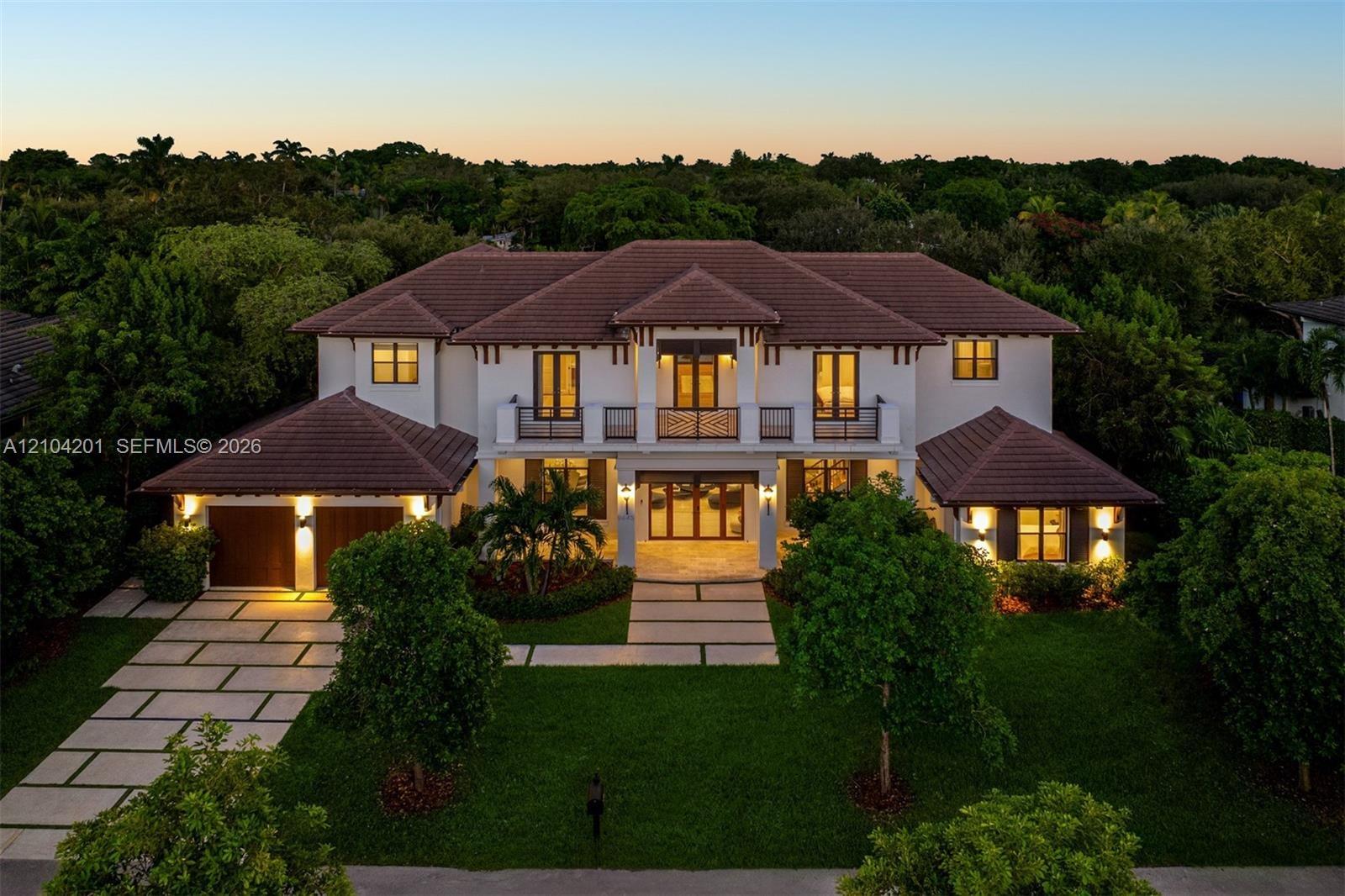 Two-story residence featuring a tile roof, stucco exterior, upper-level balcony, geometric concrete paver driveway, and an attached multi-car garage