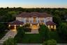 Two-story residence featuring a tile roof, stucco exterior, upper-level balcony, geometric concrete paver driveway, and an attached multi-car garage