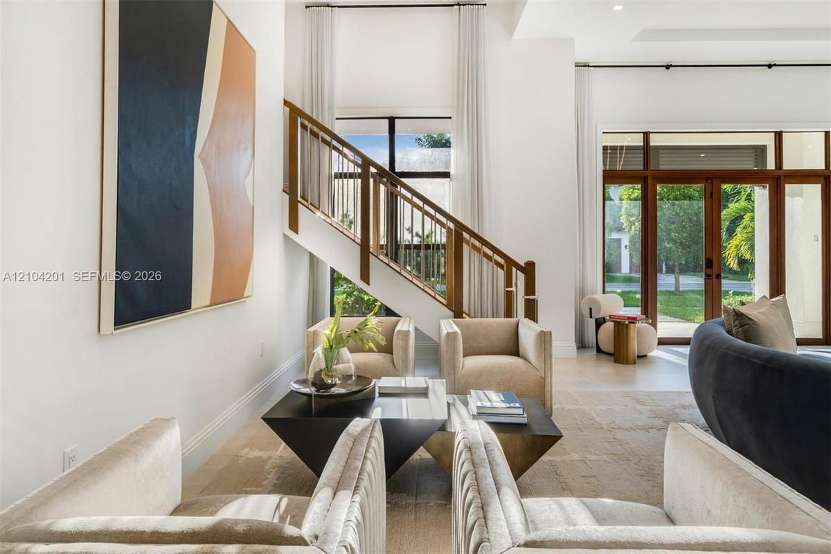 High-ceilinged room featuring a wooden staircase with metal balusters, large-format glass double doors with transom windows, and light-toned flooring