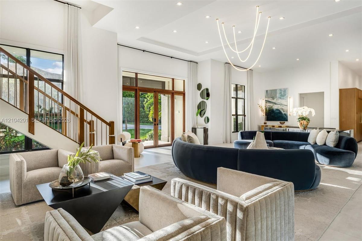 High-ceilinged room featuring a double-height staircase with wood-finish railings, recessed lighting, expansive glass-paned entrance doors, and a cust