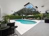 Covered outdoor patio with stone-finish tile flooring, recessed lighting, and a freeform swimming pool surrounded by a tall, mature privacy hedge