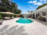 Swimming pool with a tile surround, light-toned stone patio, exterior double doors, and established greenery
