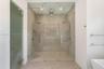 Walk-in shower featuring large-format stone-tile walls, glass-enclosed entry, dual rainfall showerheads, handheld sprayers, and textured stone-tile fl