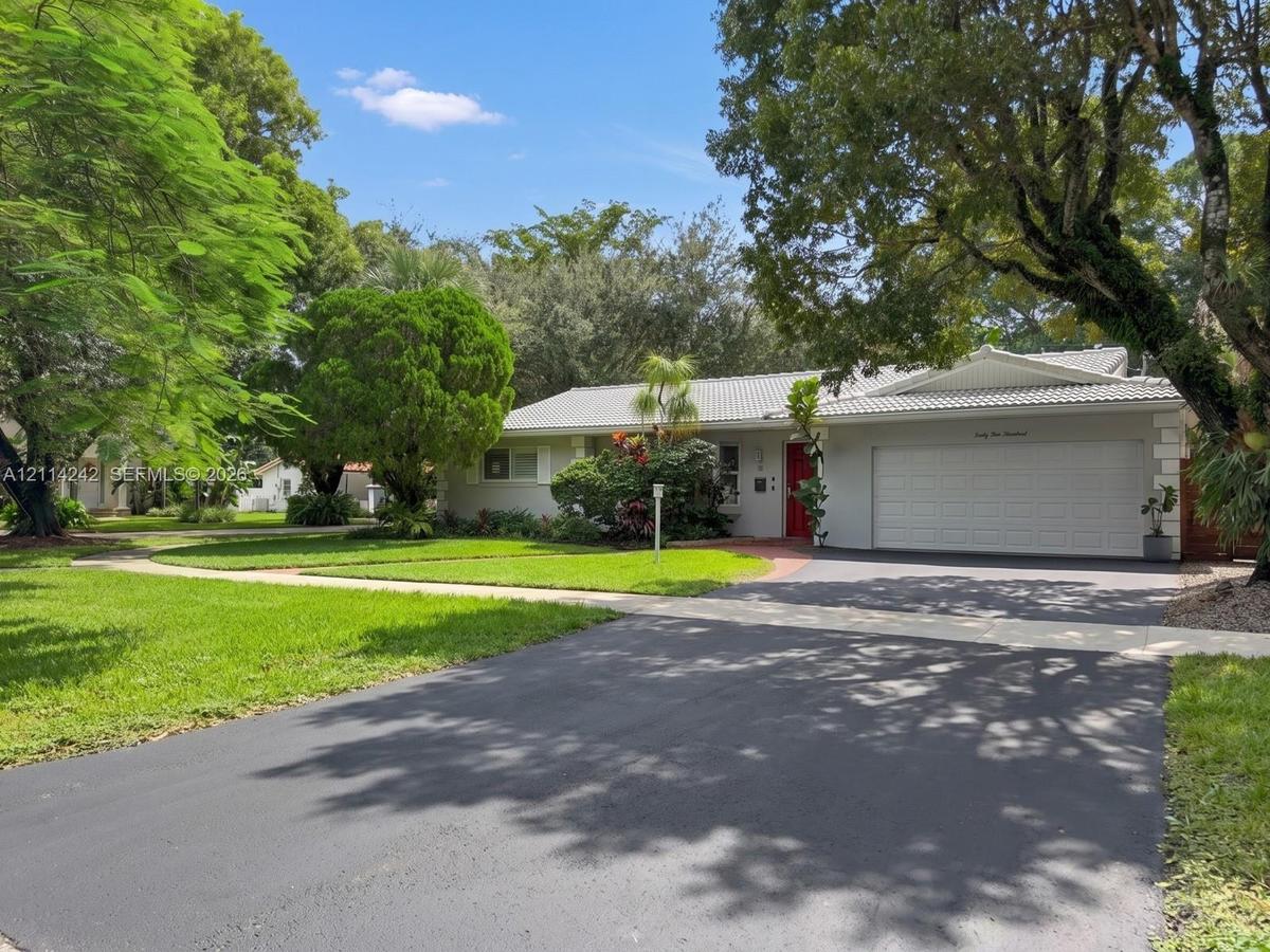Single-story exterior featuring a neutral-toned facade, expansive asphalt driveway, attached two-car garage, concrete tile roofing, and mature landsca