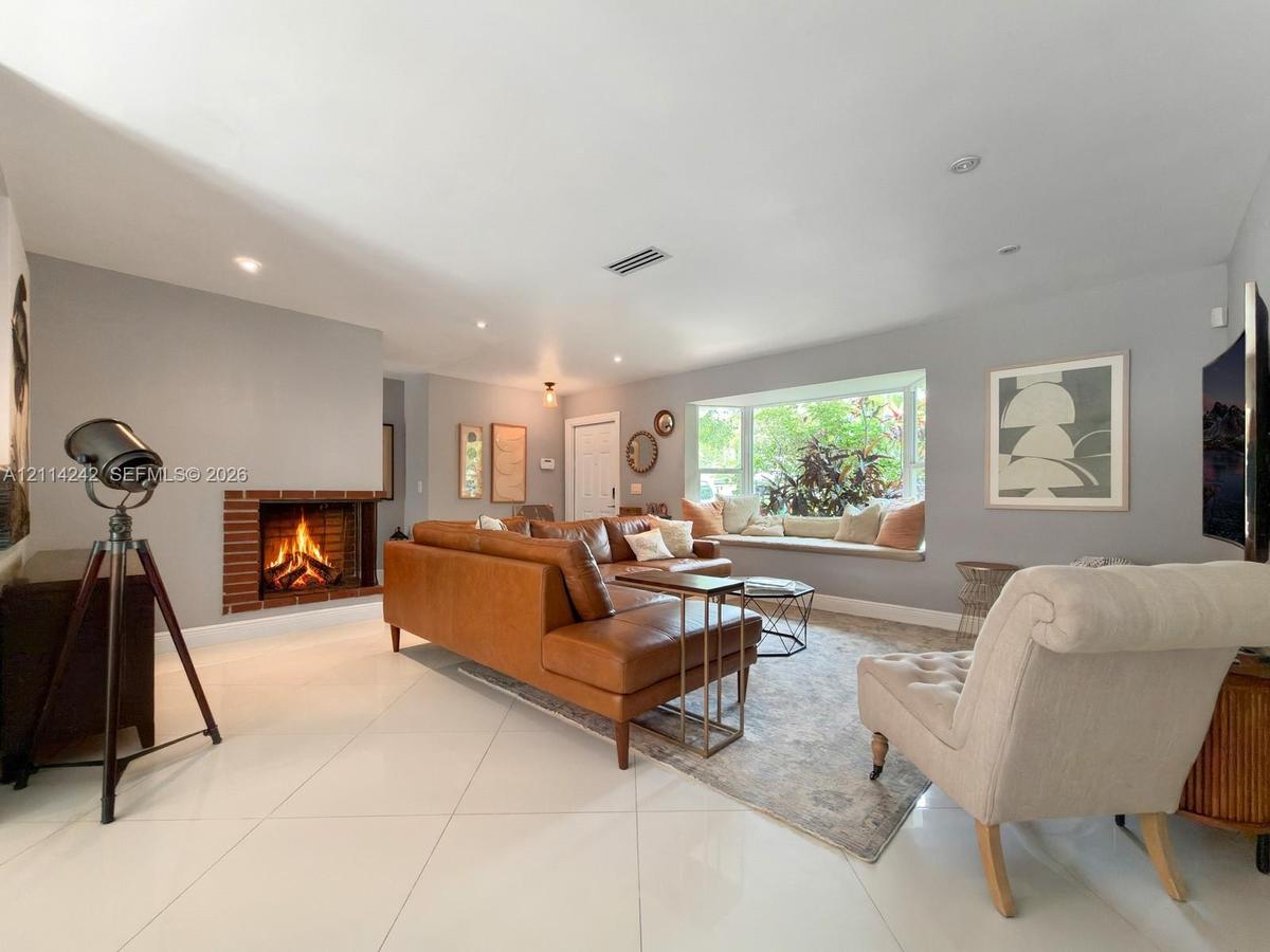 Living space featuring large-format tile flooring, a recessed fireplace with brick surround, and a bay window with a built-in bench