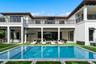 Custom swimming pool with stone coping, covered patio, second-story balcony with metal railing, and built-in outdoor kitchen