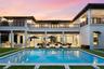 Two-story stucco exterior featuring a rectangular pool, integrated outdoor kitchen, expansive covered terrace, and decorative wrought-iron balcony rai