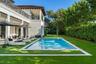 Stucco exterior featuring a second-story balcony with metal railing, an in-ground swimming pool with stone coping, and manicured landscaping