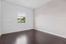 Room featuring dark wood-finish flooring, a single window, and a light-toned accent wall