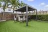 Outdoor living area featuring a covered pergola, integrated built-in grill station with a service counter, and synthetic turf lawn surrounded by matur