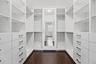 Walk-in closet featuring white built-in cabinetry, floor-to-ceiling shelving, integrated drawers with dark hardware, a center full-length mirror, and 