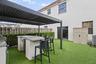 Rear patio featuring a louvered metal pergola, a built-in outdoor kitchen island with a stone-finish countertop, artificial turf surfacing, and a peri