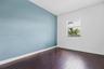 Room featuring wood-finish flooring, a vibrant blue accent wall, and a single-hung window with a roller shade