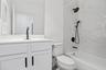 Bathroom featuring a white vanity cabinet with a solid surface countertop, matte black hardware, dual shower heads, and full-height stone-finish wall 