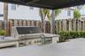 Outdoor kitchen featuring a stainless steel grill, integrated side burner, concrete-finish countertops, and a black metal pergola