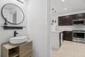 Powder room featuring a wood-finish floating vanity with a white vessel sink and matte black faucet, accented by a circular wall-mounted mirror