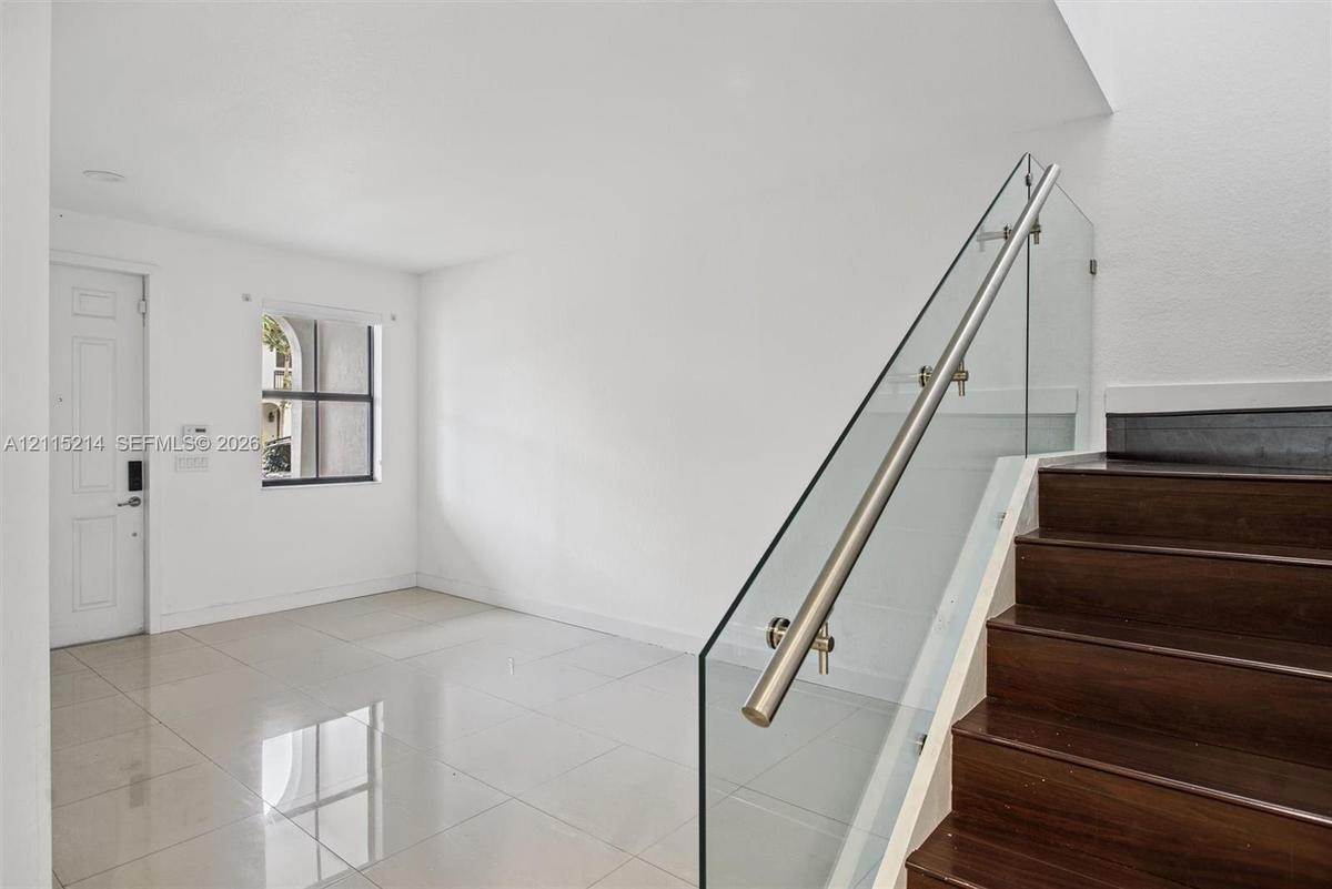 Staircase featuring dark wood-finish treads and a frameless glass railing with a metallic handrail, complemented by large-format tile flooring