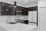 Kitchen featuring dark-toned cabinetry, white stone countertops with integrated backsplash, stainless steel appliances, stainless steel faucet with pu