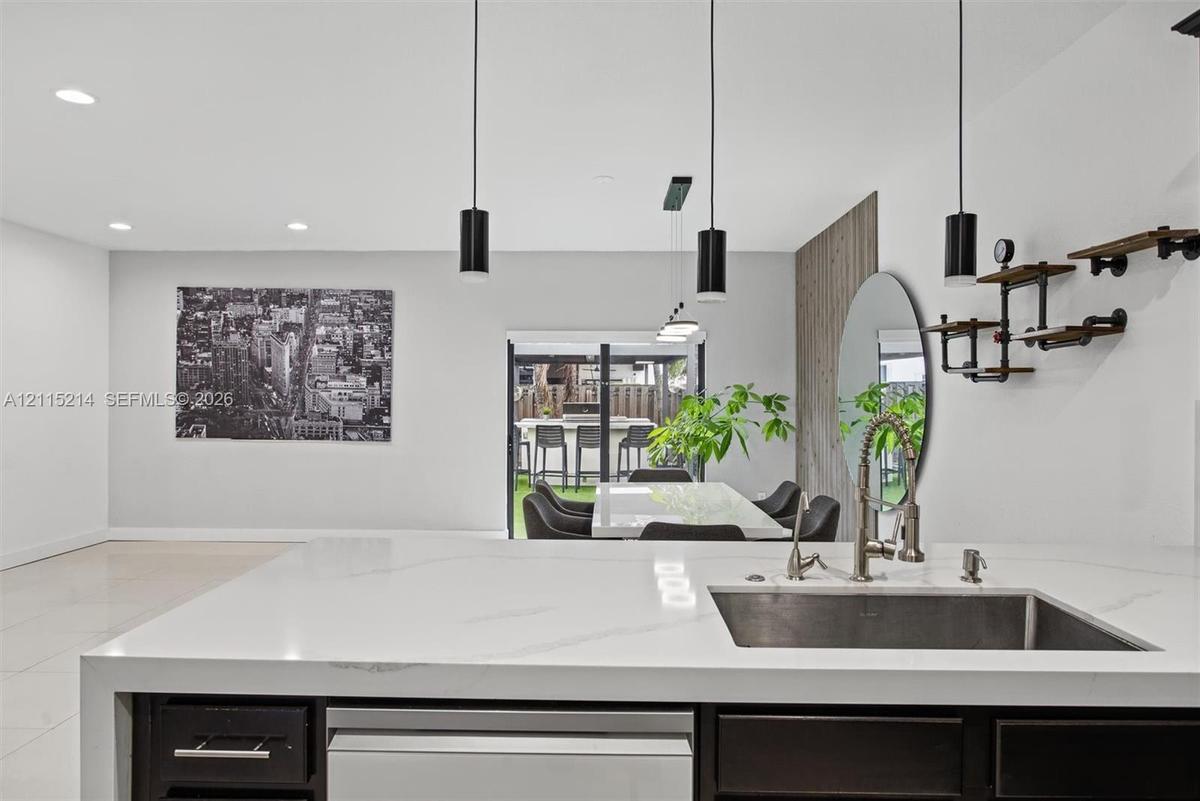 Kitchen island featuring a waterfall-edge stone countertop, undermount stainless steel sink, sleek dark cabinetry, and three pendant lights