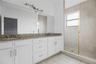 Double vanity featuring white cabinetry, stone-surface countertop, dual drop-in sinks, full-width mirror, and a walk-in shower with tiled surround and