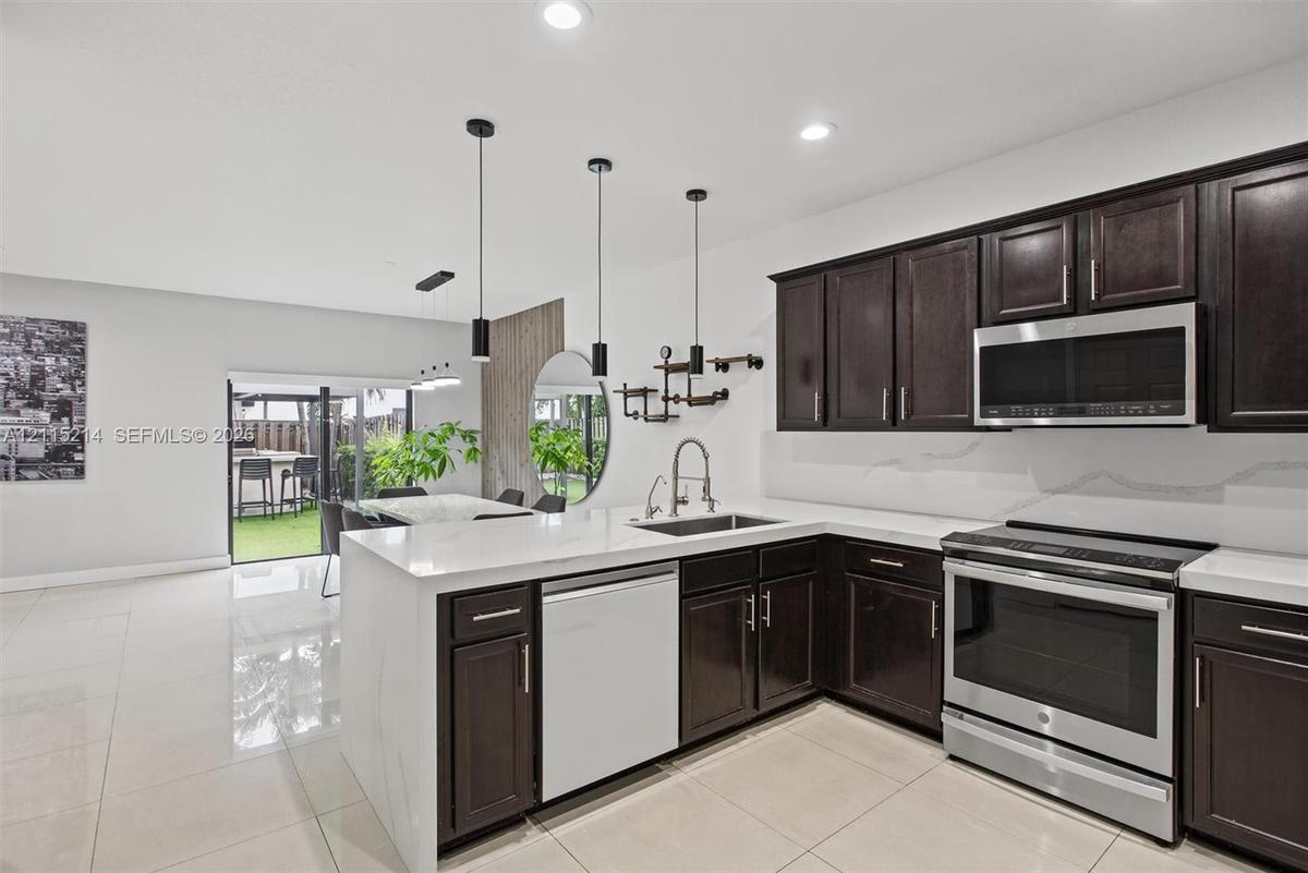 Kitchen featuring dark-finish cabinetry, white solid-surface countertops, stainless steel appliances, recessed ceiling lighting, and large-format tile