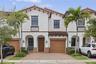Mediterranean-inspired exterior featuring stucco facade, terracotta tile roof, arched entryway, brick-paver driveway, and decorative metal railings