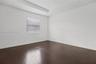 Room featuring dark wood-finish flooring, a tray ceiling, and a window with installed banded roller shades