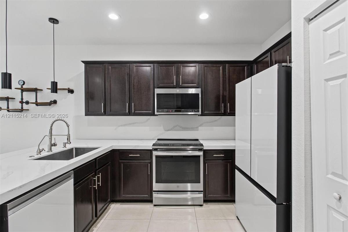 Kitchen featuring dark-finish cabinetry, stone-style countertops, stainless steel appliances, a recessed sink with a high-arch pull-down faucet, and i