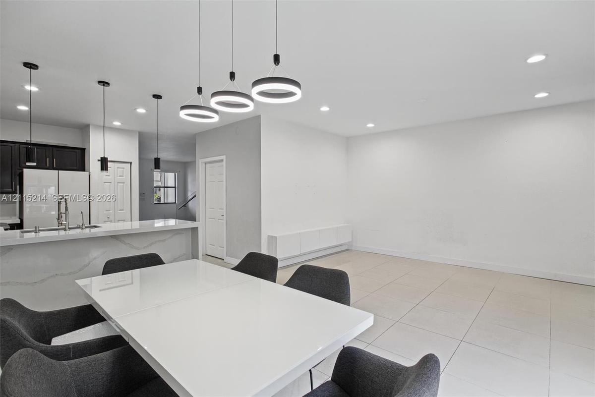 Modern open-concept area featuring large-format tile flooring, a kitchen peninsula with a stone-surfaced waterfall edge, custom pendant lighting, and 