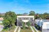 Modern two-story exterior featuring a light-toned stucco facade, horizontal slat privacy screening, double glass balcony doors, and a linear stone-pav