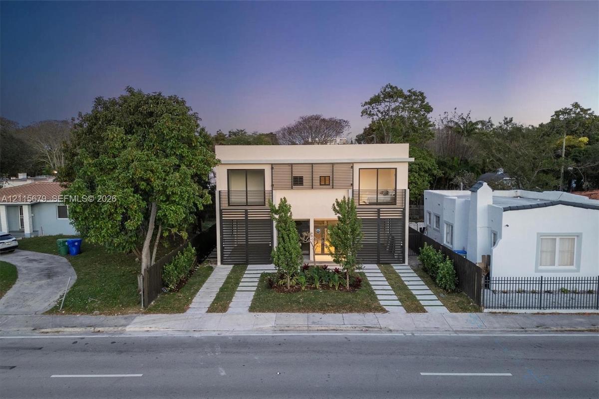 Two-story modern architectural exterior featuring a smooth stucco facade, black metal privacy screening, sliding glass balcony doors, and dual concret