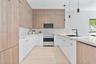 Kitchen featuring two-tone cabinetry with wood-finish upper cabinets and high-gloss lower cabinets, quartz countertops, stainless steel range with ove