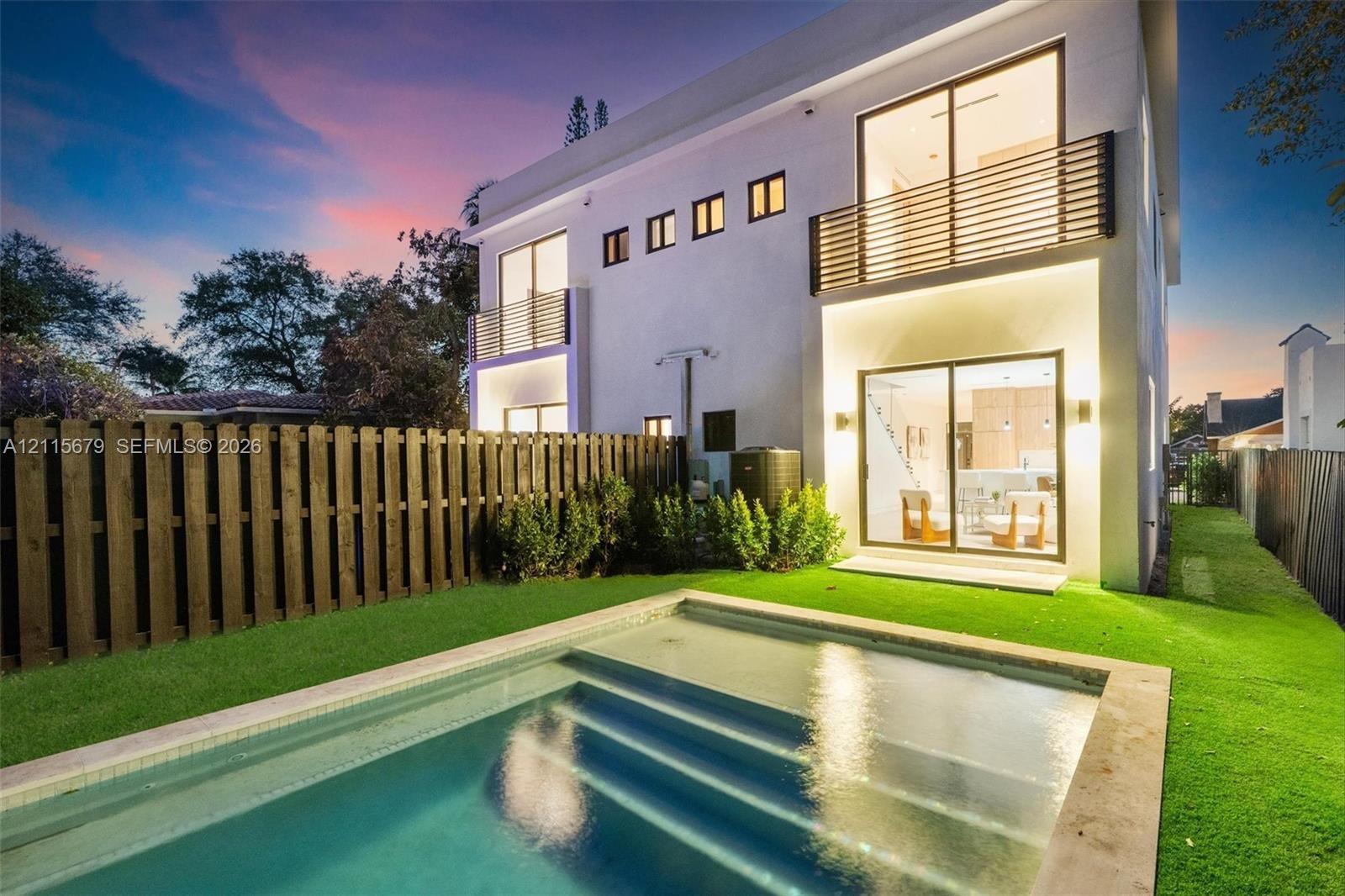 Two-story exterior with stucco finish, in-ground swimming pool, horizontal slat balcony railings, sliding glass doors, and privacy fencing