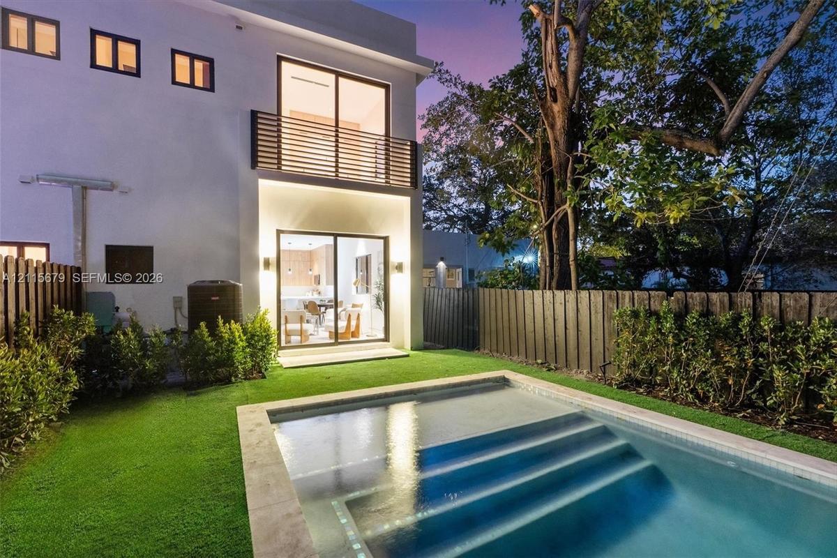 Modern exterior featuring a swimming pool with integrated stairs, synthetic lawn, wood-slat upper balcony railing, and floor-to-ceiling sliding glass 