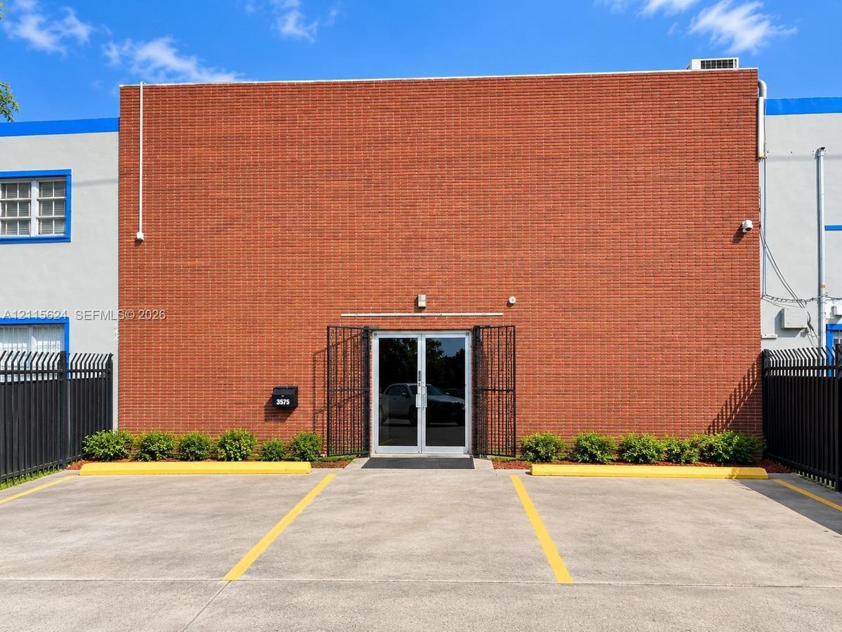 Exterior facade featuring red masonry brick construction, double-glass entry doors with security grilles, dedicated concrete parking space, and perime