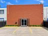 Exterior facade featuring red masonry brick construction, double-glass entry doors with security grilles, dedicated concrete parking space, and perime