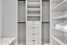 Custom walk-in closet featuring white built-in shelving, four integrated storage drawers, and multiple hanging sections