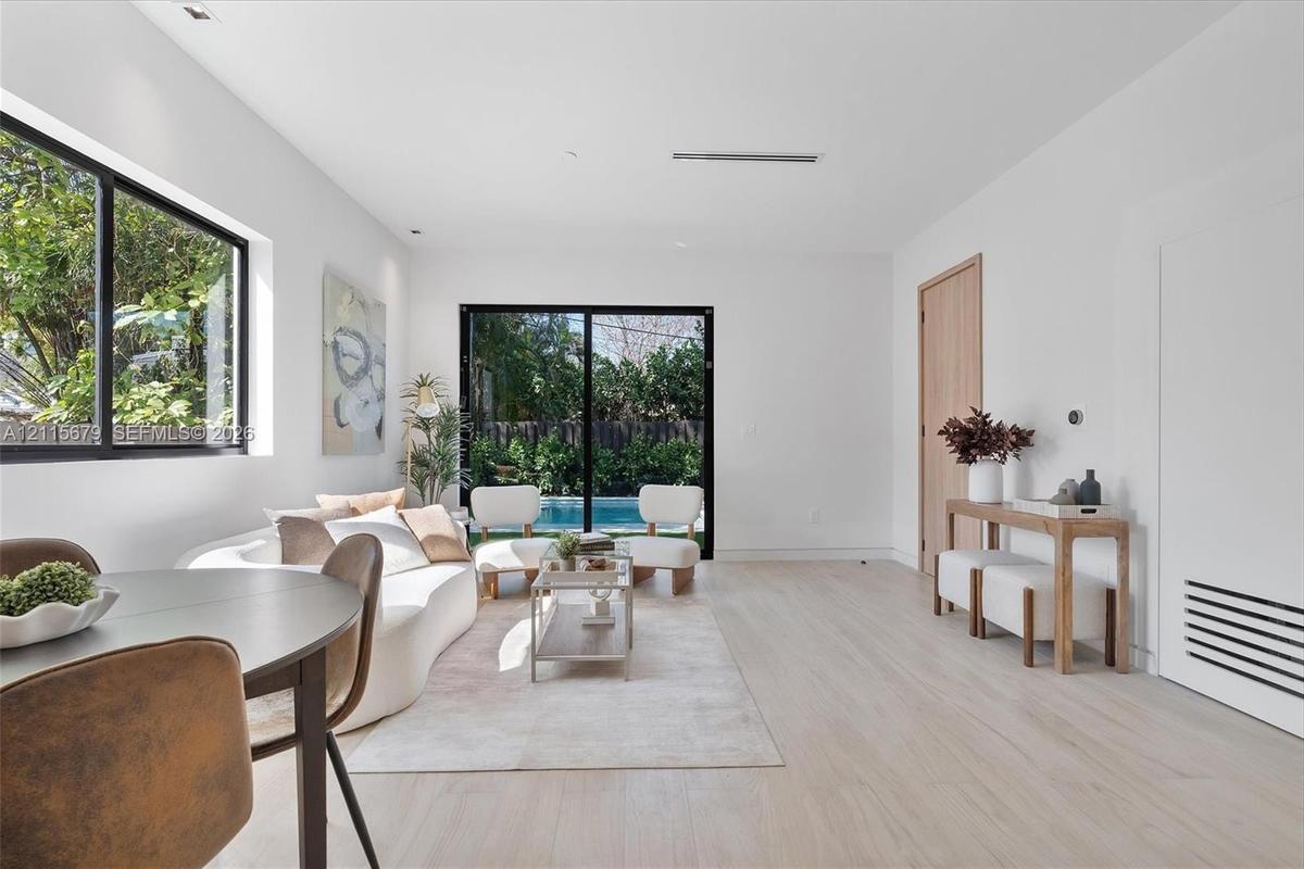 Open-concept interior featuring light wood-finish flooring, recessed lighting, expansive black-framed windows, and sliding glass doors with exterior p