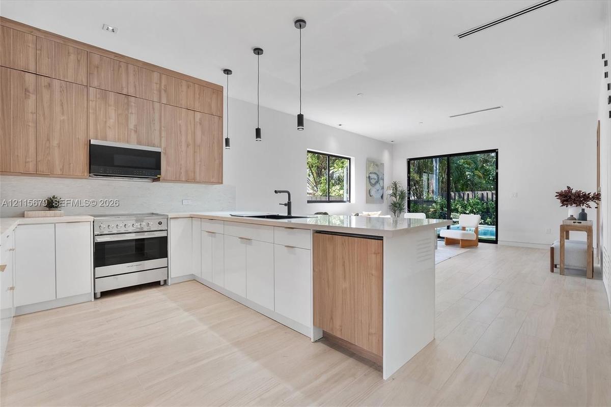 Kitchen featuring two-tone wood-finish and matte white cabinetry, stone-surfaced island, stainless steel range with overhead microwave, and wood-finis
