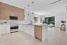 Kitchen featuring two-tone wood-finish and matte white cabinetry, stone-surfaced island, stainless steel range with overhead microwave, and wood-finis