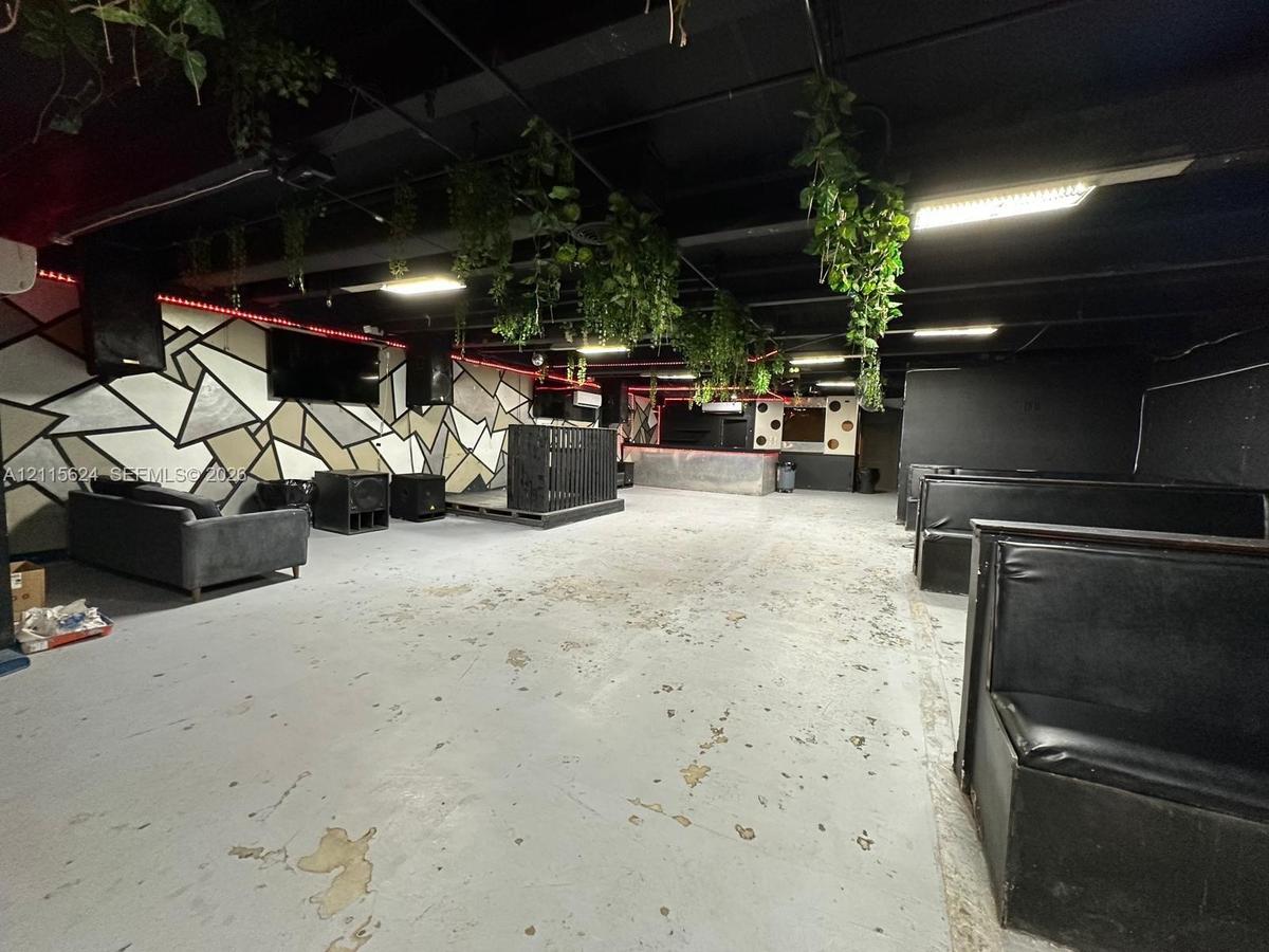 Open-concept interior featuring industrial-style exposed ceiling, geometric wall mural, built-in elevated platform, and permanent perimeter banquette 