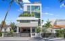 Modern multi-story exterior featuring floor-to-ceiling windows, multiple glass-railed balconies, a gated entrance, and a covered ground-level parking 