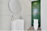 Wall-mounted circular mirror, white vanity with fluted cabinetry, polished chrome faucet, floor-to-ceiling green glazed tile accent wall, and porcelai