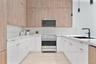 Kitchen featuring floor-to-ceiling wood-finish cabinetry, gloss white lower cabinetry, light-toned stone-finish countertops, stainless steel gas range